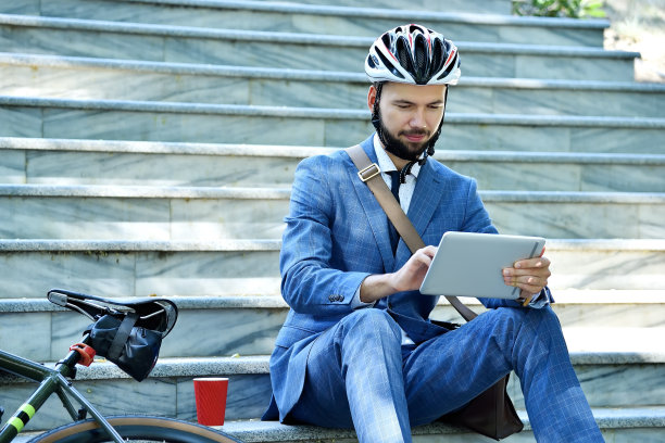 戴着头盔的商人坐在楼梯上，分析数字平板电脑上的报告。图片下载