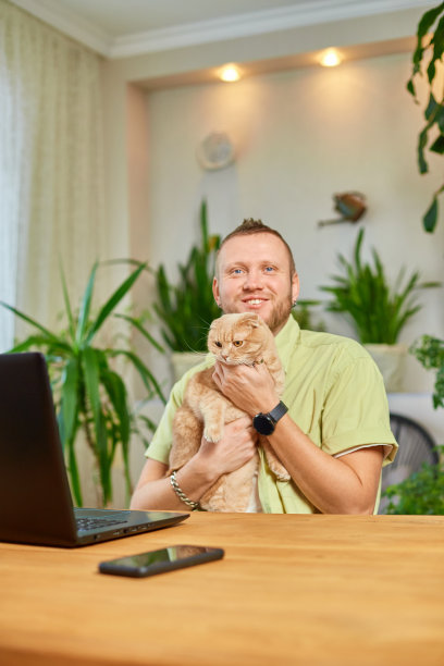 一个男人正在用一个黑色的笔记本，笔记本电脑和一只猫躺在他的手上图片下载