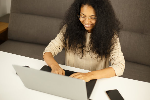 一个快乐的黑人妇女，带着欢快的露齿微笑，在笔记本电脑键盘上打字。年轻的成年女性在禁闭期间在家用现代笔记本电脑工作。企业家在网上做远程工作图片下载