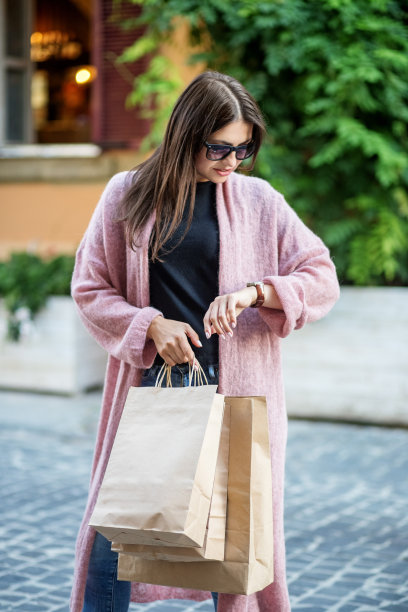 一个小女孩看着她的手表，拿着纸袋。概念生活方式、购物、旅游、时间图片下载