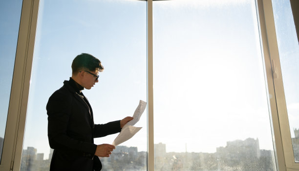 成功的商人在全景窗口旁阅读一份纸质文件。深思熟虑自信的年轻自由职业者在家里做文书工作学习正式信函。图片下载