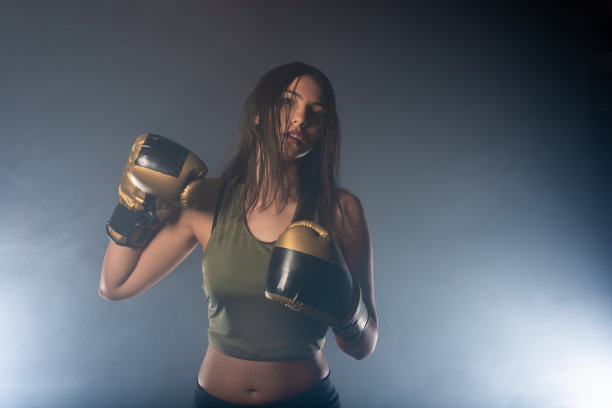 这是一个自信的年轻运动女孩，戴着拳击手套，在烟雾缭绕的背景下摆姿势图片下载