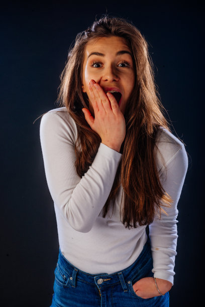 一名年轻女子在黑色背景下摆姿势，同时做出一个令人惊讶的手势(哇效果)。图片下载