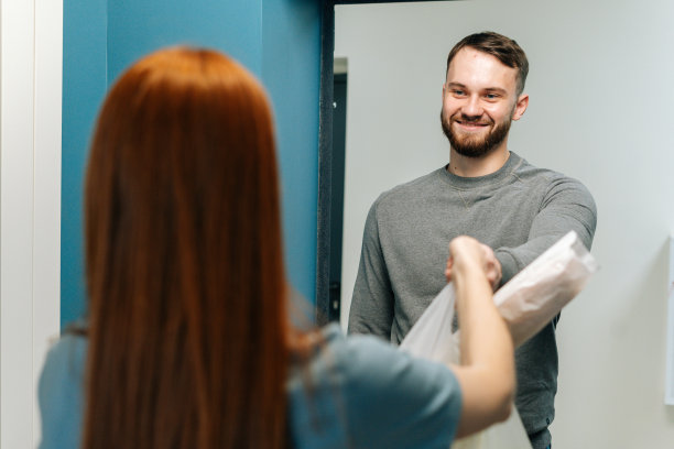 快乐的大胡子快递男送杂货袋与陌生的家庭主妇在门口的顾客。图片下载