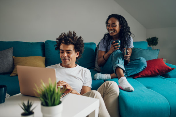 一对非洲裔美国夫妇在家里的沙发上放松着笔记本电脑和咖啡图片下载