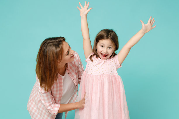穿着粉红色衣服的快乐女人有一个5-6岁的有趣的孩子。妈妈，小孩，女儿做赢家的姿态庆祝孤立在柔和的蓝色背景工作室母亲节爱家庭的概念图片下载