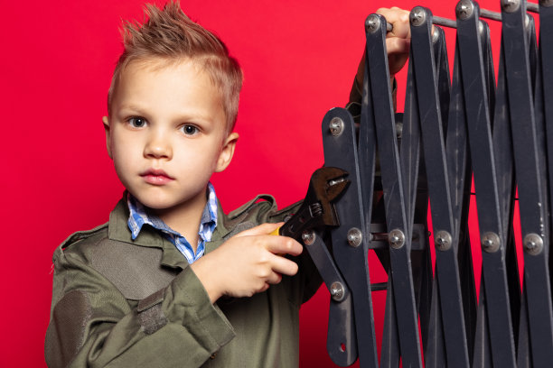 小工人。可爱的学龄前男孩，穿着工装裤的汽车修理工或装配工的形象，红色背景上的工作工具正在修理。图片下载