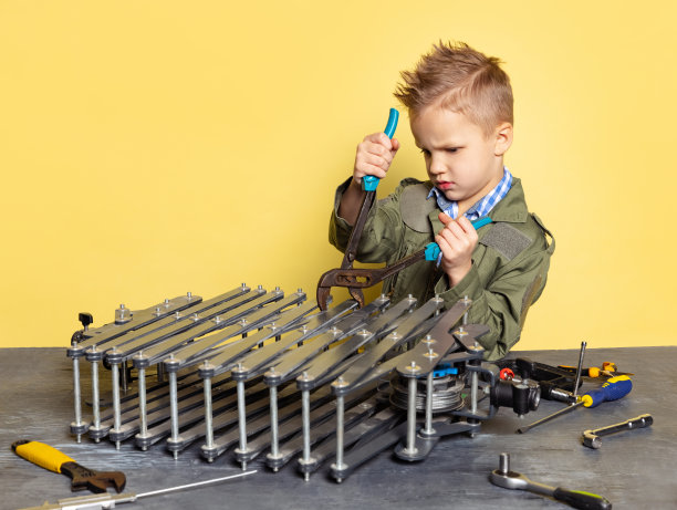 可爱的小男孩，穿着工装裤的汽车修理工或装配工的形象，在黄色的背景上用工具修理汽车发动机。图片下载