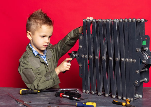 小工人。可爱的学龄前男孩，穿着工装裤的汽车修理工或装配工的形象，红色背景上的工作工具正在修理。图片下载