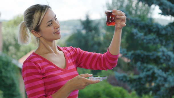 阳台上，金发的年轻女子一边喝着热茶，一边欣赏着绿色的景色。图片下载