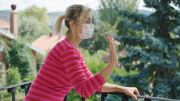 这位金发年轻女子在阳台上为支持抗击冠状病毒的人们鼓掌。图片下载