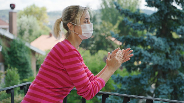 这位金发年轻女子在阳台上为支持抗击冠状病毒的人们鼓掌。图片下载