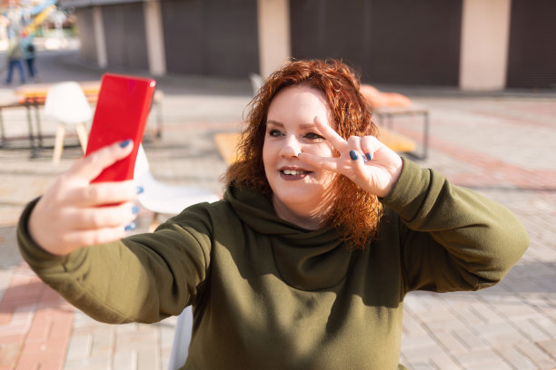 一个微笑的胖女人用她的手机自拍的肖像。博客和社交媒体营销的概念图片下载