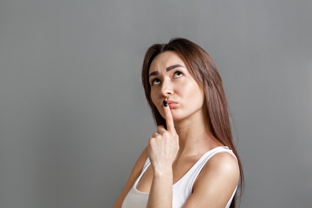 寻找思想和信息的概念。一个沉思的年轻白人妇女的肖像，看着顶部，把她的手指放在她的嘴。灰色的背景。本空间图片下载