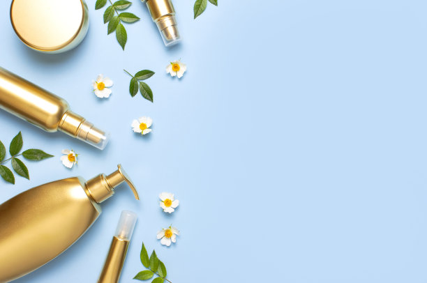 化妆假金瓶。化妆品，春天白色的花朵绿色的叶子在蓝色的背景上。化妆品春夏概念。平躺顶视图复制空间。品牌产品，美容背景图片下载