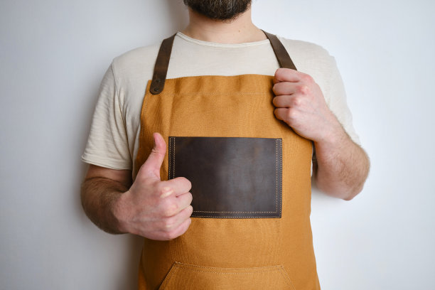一个穿着厨房围裙的男人。厨师负责烹饪。穿着制服和防护服做饭。食品服务的工作。专业烹饪。驼色面料围裙，休闲时尚服装。英俊的贝克摆姿势图片下载