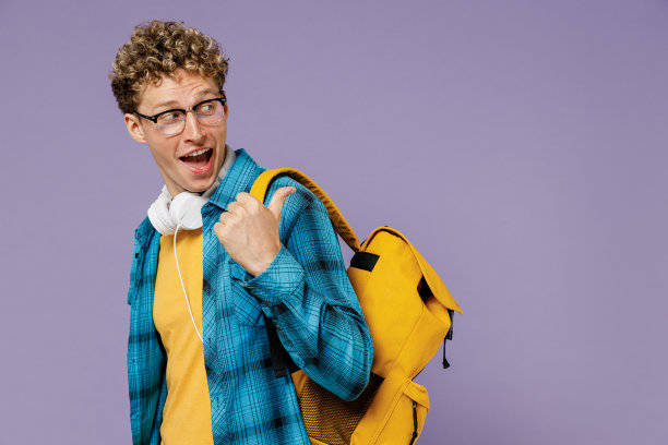 年轻的侧视图男孩十几岁的学生在休闲衣服背包耳机眼镜看一边的工作空间区域孤立在紫罗兰色背景工作室教育在高中大学的概念图片下载