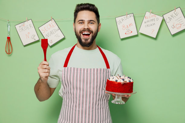 年轻的满意的快乐的乐趣男厨师糖果师面包师男人穿条纹围裙抱装饰生日甜甜点蛋糕孤立在素色淡绿色背景工作室。烹饪食物的概念图片下载