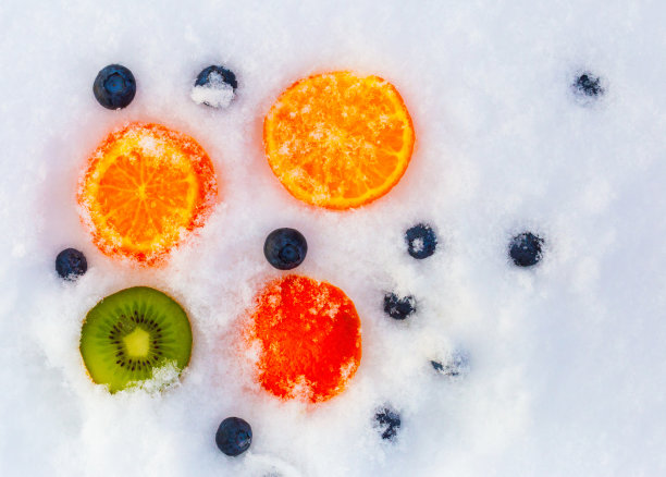 新鲜的绿色猕猴桃片，多汁的橘色橘子和蓝莓被白色寒冷的冬雪包裹着。明亮的彩色背景照片。水果沙拉包装设计理念图片下载