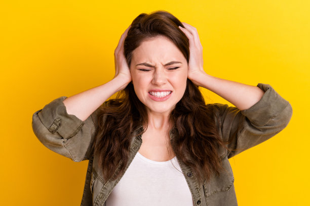 照片中年轻女子穿着棕色衬衫，手指，手，耳朵，孤立的黄色背景图片下载