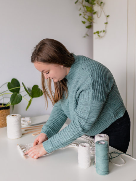 一个女人在她的房子里编织。天然棉线和木珠。手工编织腰带在工作过程中。女性的爱好。图片下载
