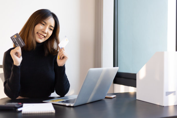 快乐微笑的亚洲妇女在办公室拿着信用卡。金融和网上购物概念。素材图片