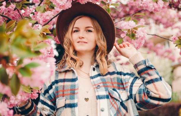 年轻时尚的女子站在樱花公园，享受美丽的粉红色。春天女人在樱花盛开的概念。美丽的金发女人长头发户外。樱花。特写肖像。图片下载