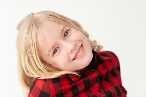 一个微笑的金发少女的特写镜头，她的头斜靠在工作室的白色背景上图片下载