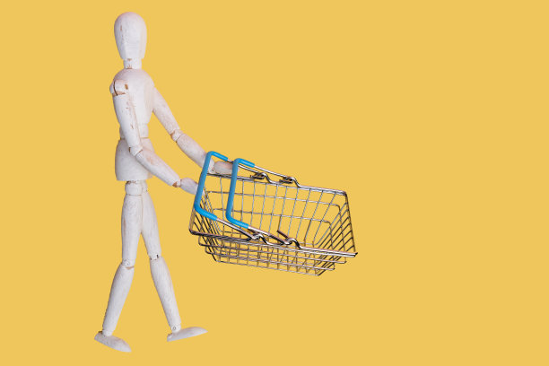购物车与木制人人体模型购物袋在黄色背景。网上购物创意，超市概念。本空间图片下载