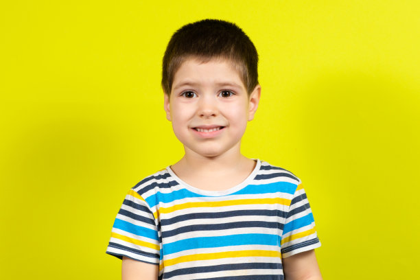 一个微笑的英俊的棕色头发的4岁男孩的肖像在黄色背景上的条纹蓝色t恤，复制的地方为文本图片下载