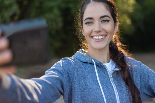 美丽的女人在模糊的背景下用手机自拍图片下载