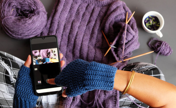 女子手戴蓝色连指手套钩针，在深色基调上为礼物织紫罗兰色毛衣图片下载