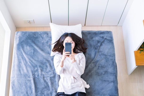年轻女子在床上使用智能手机图片下载