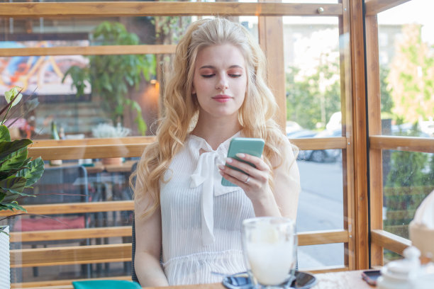 在咖啡厅休息时，迷人的女人微笑着在手机上读好消息图片下载