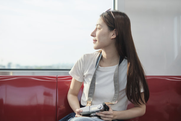 亚洲女性游客在公共列车上坐观光城市窗口。图片下载