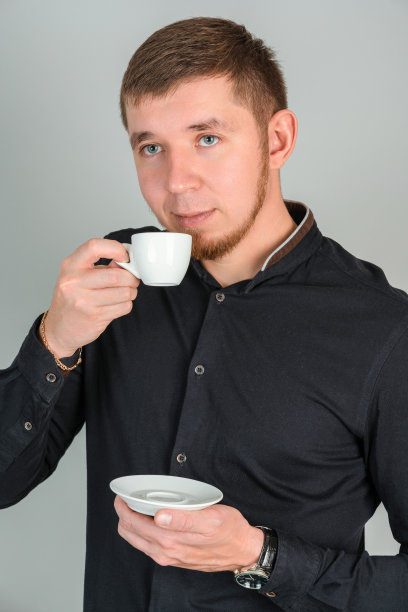一个英俊的大胡子男人用一个白色的小杯子喝咖啡，目光移开图片下载