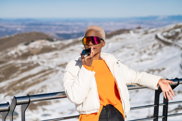 一位非洲裔美国妇女在冬天的雪山上靠在篱笆上打电话图片下载