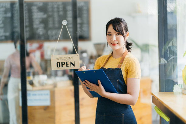 一个快乐的女服务员站在餐厅门口的肖像。一个成熟的商业女性在她的咖啡店接待新顾客的肖像。快乐的女老板在她的小商店里展示着开放的标志。图片下载