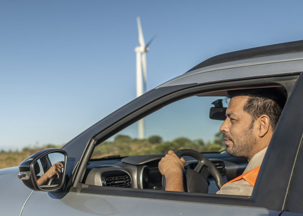 带着防护设备的电气工程师坐在一辆移动的车里前往风力发电厂。图片下载