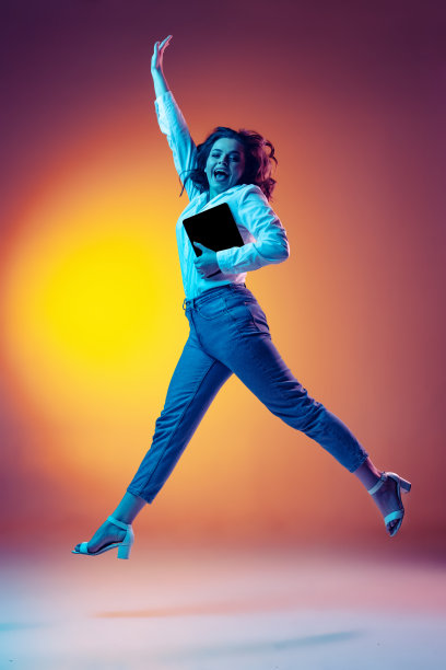 快乐的年轻美丽的女孩长卷曲的头发跳跃的全长肖像孤立在橙色的背景霓虹灯，滤镜。情感、美、时尚的概念图片下载