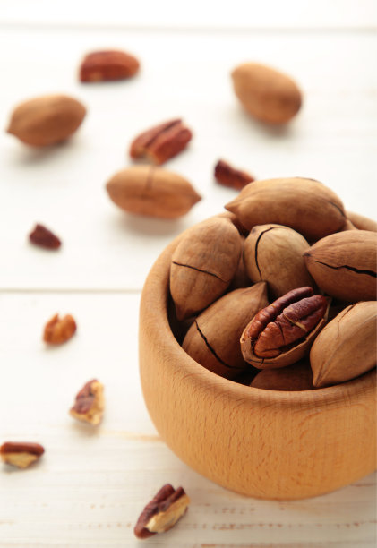 新鲜美味的山核桃木碗上白色背景。完整的和有裂缝的山核桃。垂直的照片。图片下载