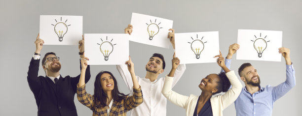 跨种族的同事们手持白色的灯泡，象征着一种新想法。图片下载