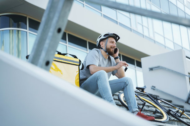 快送外卖的快递员坐在楼梯上，带着保温包和自行车。图片下载