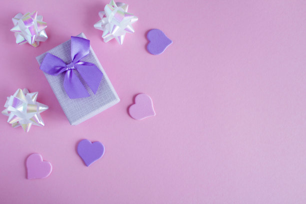 礼品盒系紫色蝴蝶结和心在粉红色的背景。前视图。副本的空间。图片下载
