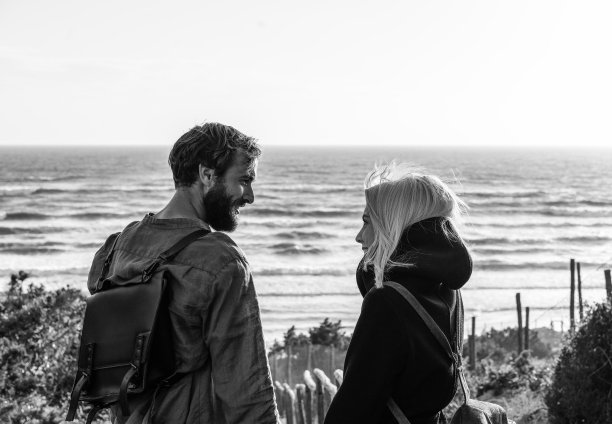 浪漫幸福的情侣站在沙丘上的木梯上，在大海前的荒野沙滩上-男朋友和女朋友背着复古的背包在日落时看着对方的眼睛图片下载