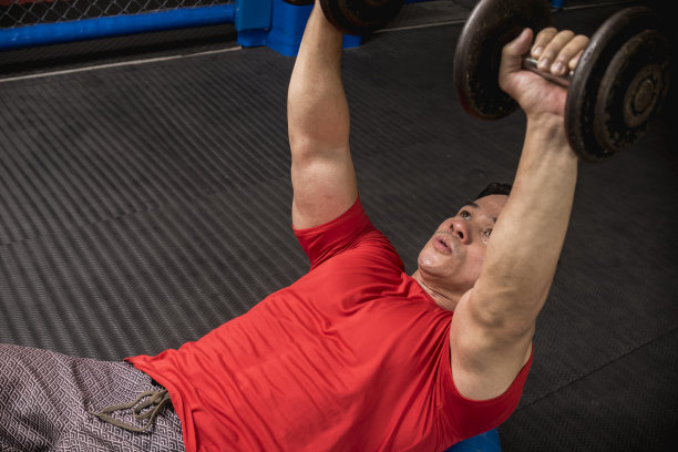 一个健康和运动的亚洲人做哑铃压在稳定的球。在健身房做胸部锻炼。图片下载