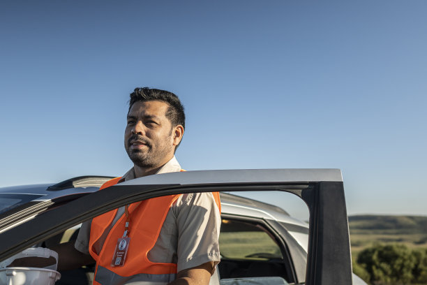 一个带着防护设备的电气工程师从一辆电动汽车里出来，在一个风电场公园里图片下载