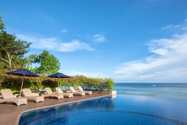 热带海洋旁的木质阳台露台上有躺椅和雨伞图片下载