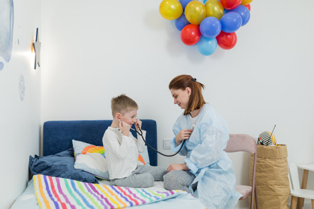 年轻的女医生在家治疗一个生病的孩子，一个小男孩。用听诊器听，看喉咙。图片下载