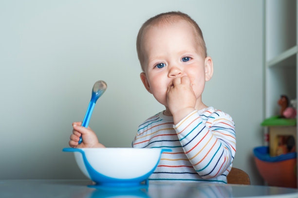 蹒跚学步的小男孩在桌子上用勺子吃饭。图片下载